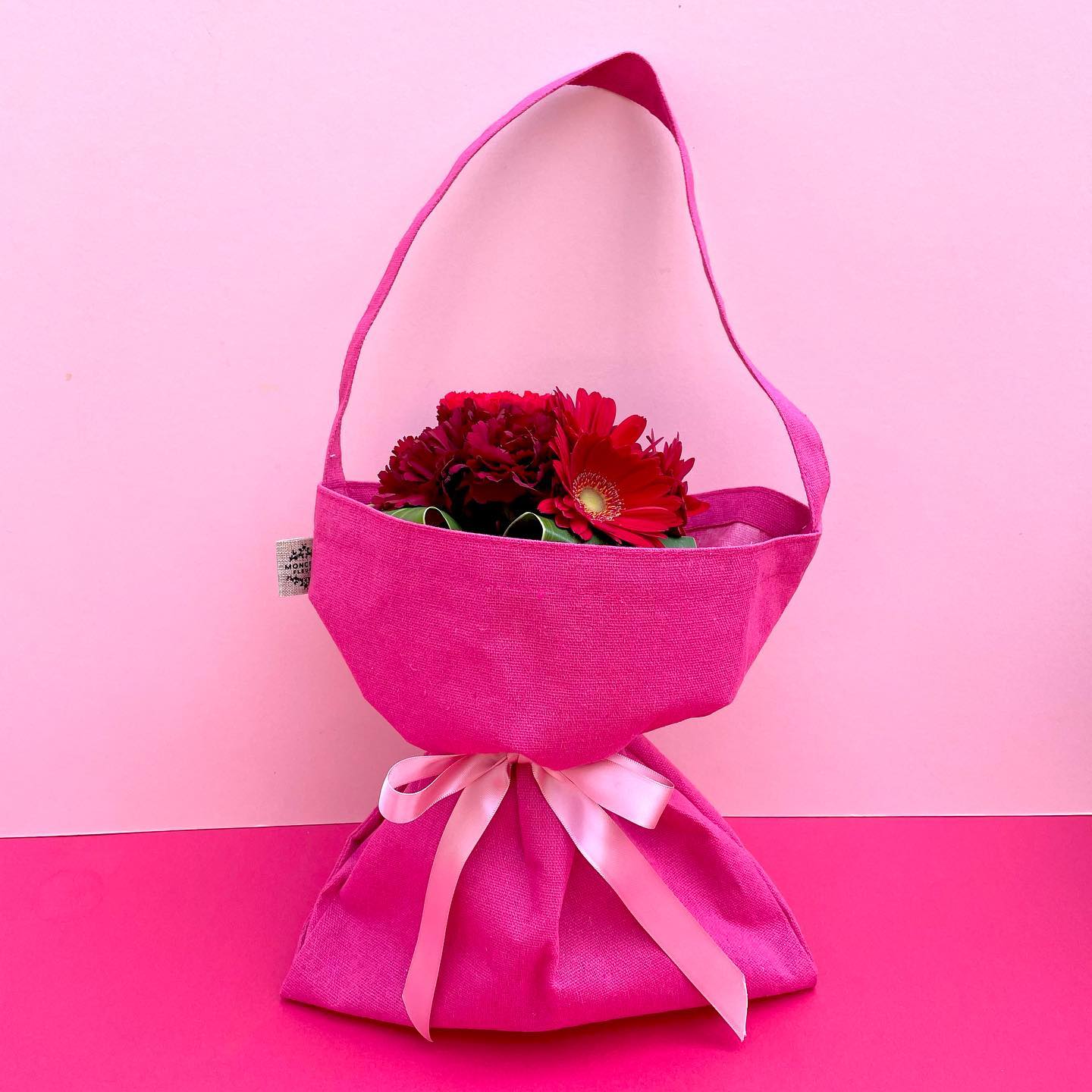 Happy Mother’s Day!

＊＊＊＊＊＊＊＊＊＊＊＊
D.Espoir Rouge
¥3,850（送料別）

母の日の主役・カーネーションに「感謝」「希望」の花言葉を持つガーベラをプラス！

カーネーションとガーベラのブーケを、ボタンで長さを変えられる花束用エコバッグでラッピングしました。

中にはお水代わりのゼリーが入ったプラスチックの花瓶付き。
ラッピングしたまま飾って楽しんでいただけます。

エコバッグの内側は防水加工になっていて、長い丈のお花のお買い物の時に便利！

一部の店舗を除いたモンソーフルール店舗では、来年の母の日前日まで、こちらのエコバッグを持ってきた方、切花がなんと10％OFF！いつでも、何度でもOK！こちらの袋に入らないサイズのお花でも、もちろんOKです♪
（ただしご自宅用に限ります）

母の日当日だけでなく、365日お花のある生活をお母さんにプレゼントしませんか？

サイズ：φ15㎝、高さ25㎝